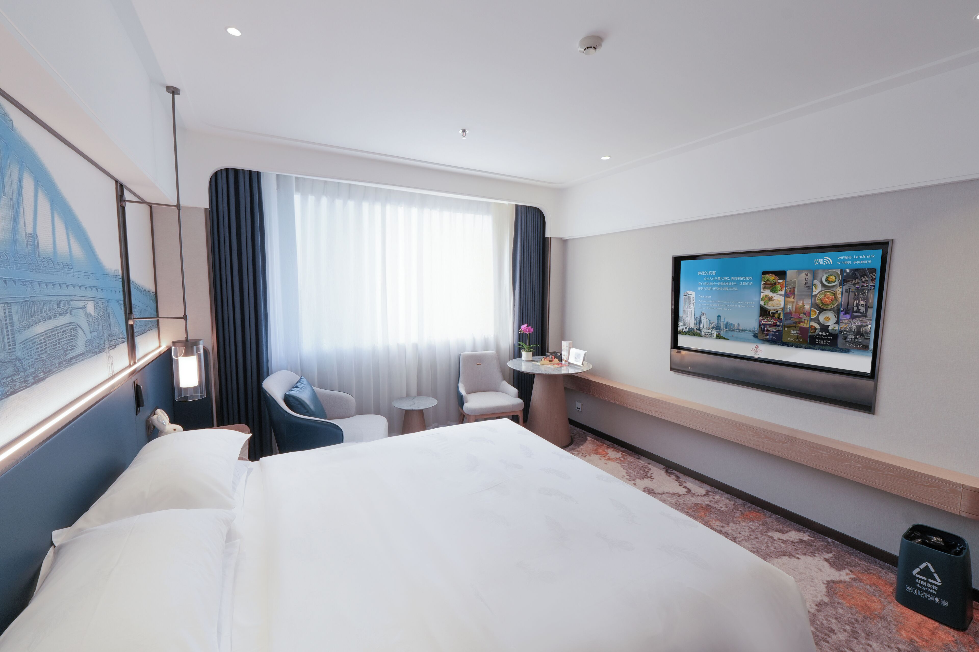 Een hotelkamer met een groot bed, een bureau, een stoel, een tafeltje, een aan de muur bevestigde televisie en een raam met gordijnen.
