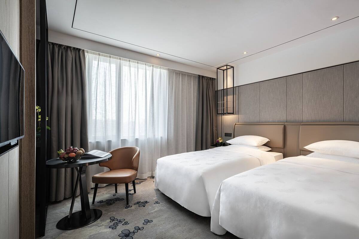 A hotel room with two beds, a desk with a chair, a TV, and a bedside table with a lamp.