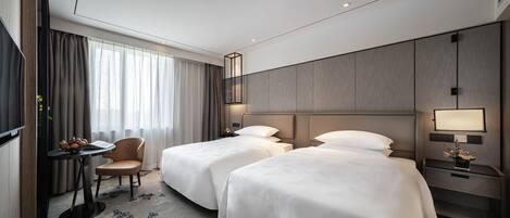 Habitación de hotel con dos camas, un escritorio con silla, un televisor y una mesita de noche con lámpara.