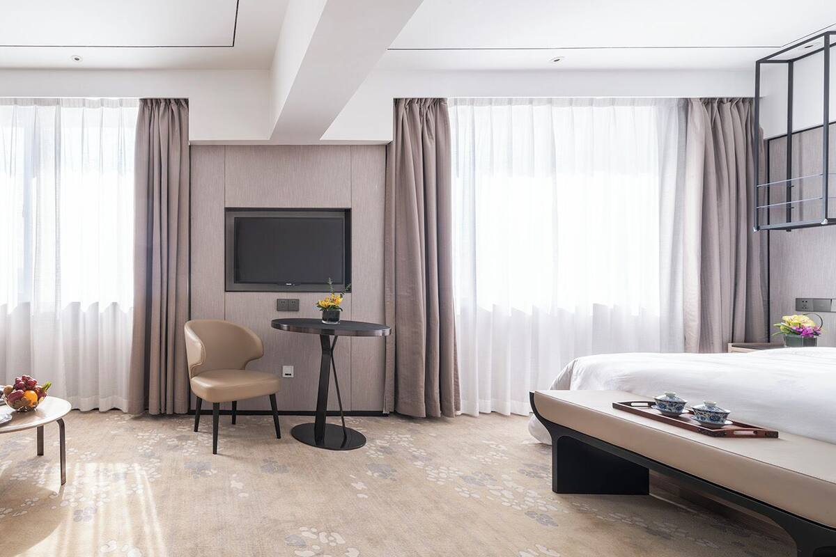 A modern hotel room with a bed, a sofa, a chair, a small table, and a TV.