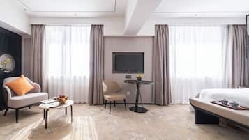 A modern hotel room with a bed, a sofa, a chair, a small table, and a TV.