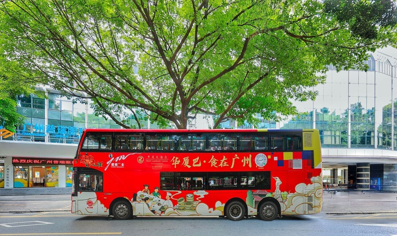 Un autobús rojo de dos pisos con anuncios en los laterales, estacionado frente a un edificio con un árbol grande.
