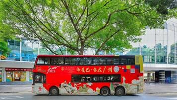 A red double-decker bus with advertisements on its side, parked in front of a building with a large tree.