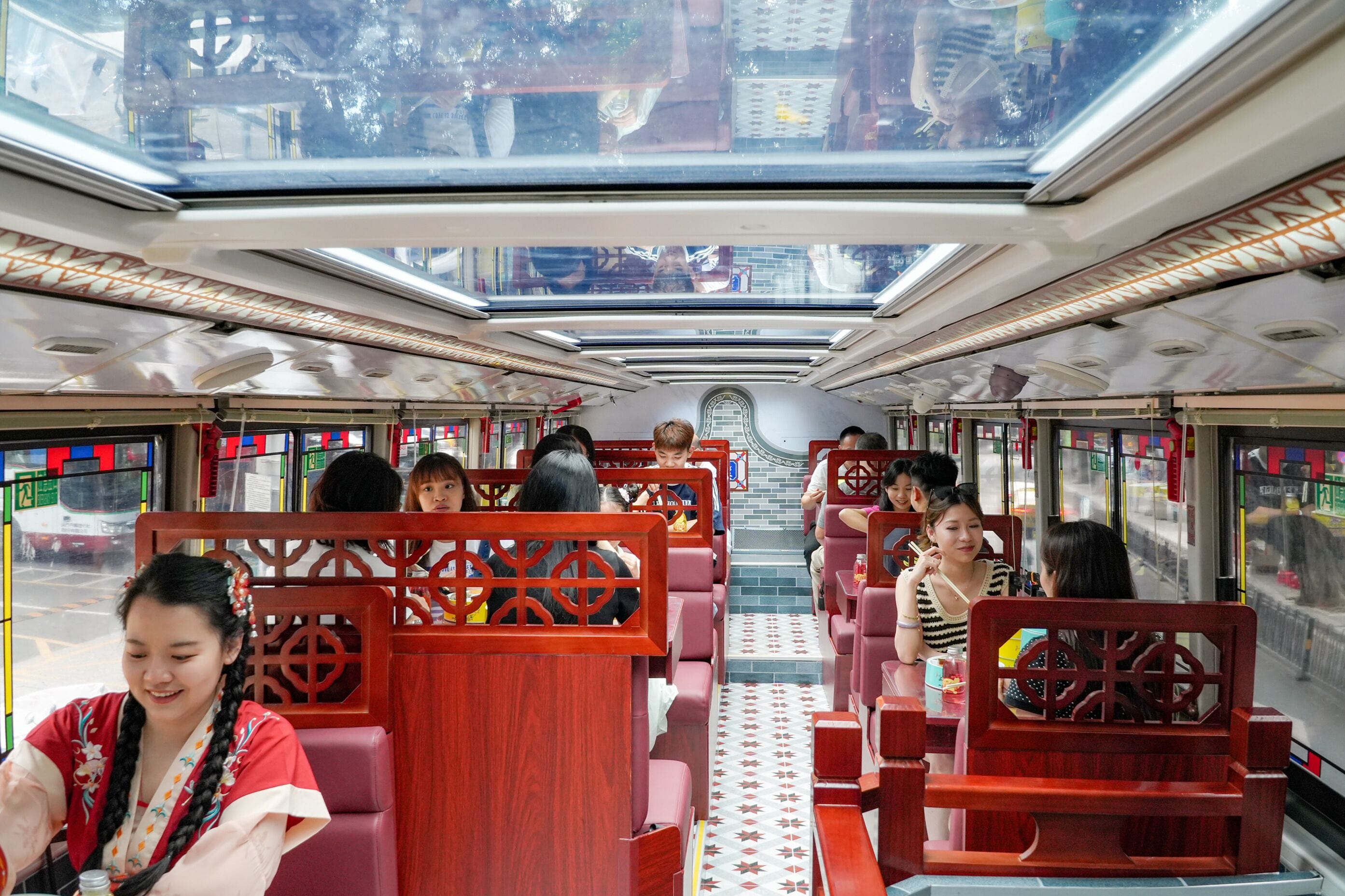 A train interior with passengers seated, overhead windows, and a central aisle.