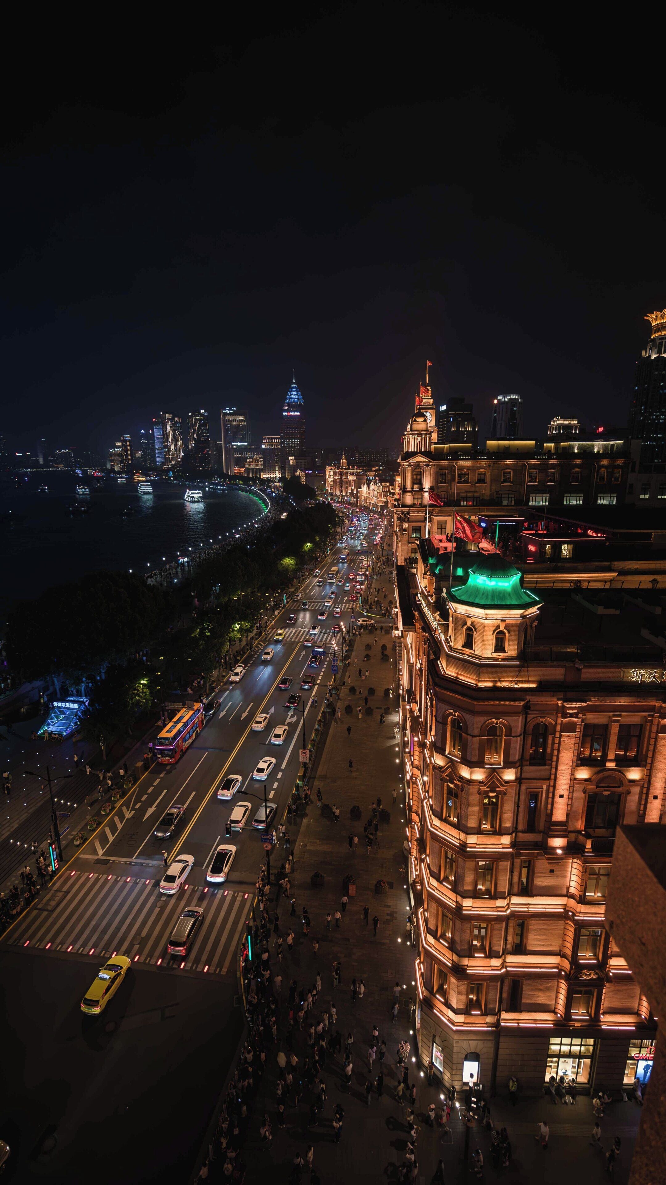 A nighttime cityscape with a prominent building featuring a green-lit dome and a busy street with vehicles and pedestrians.