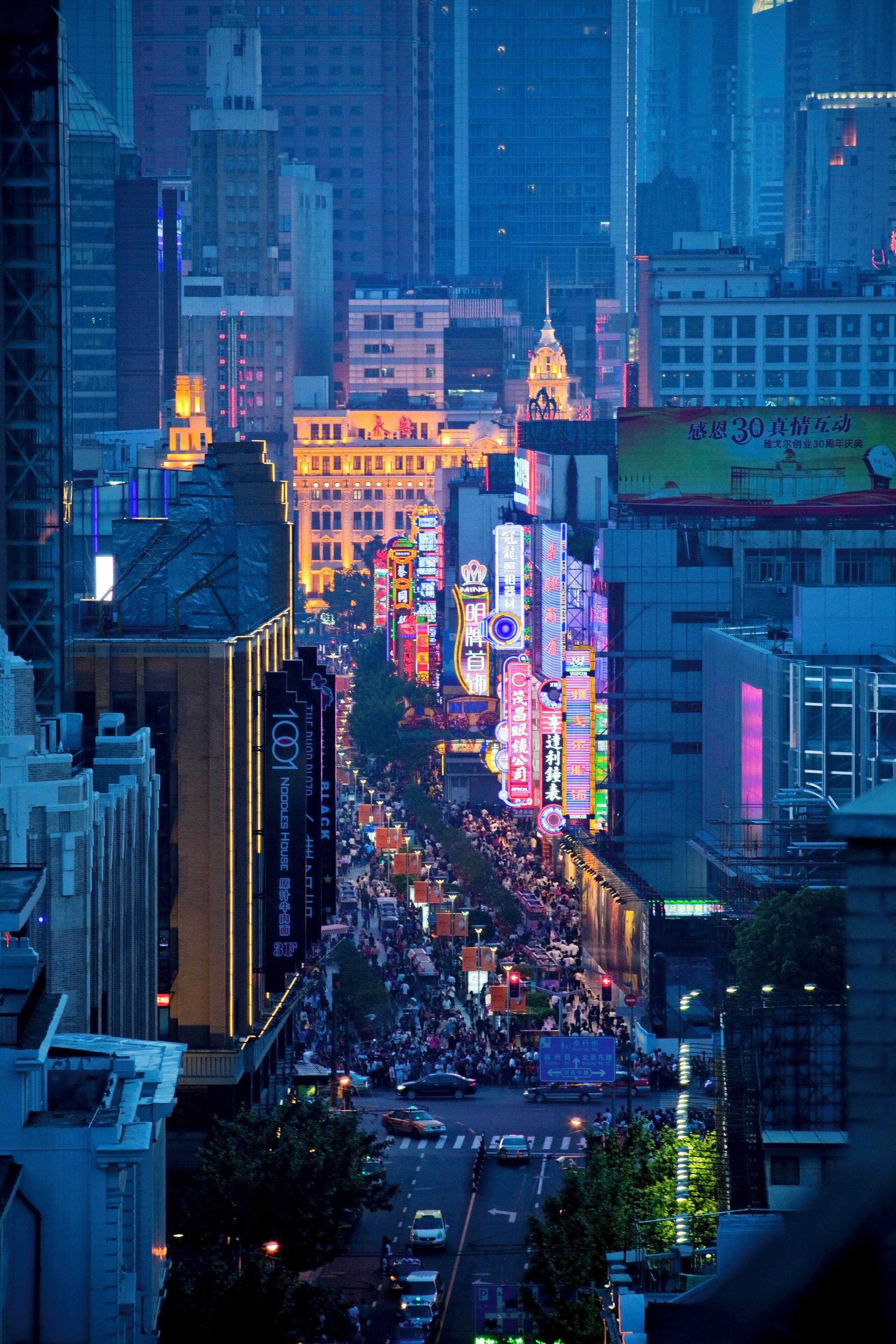 A cityscape at night with illuminated billboards and a busy street.
