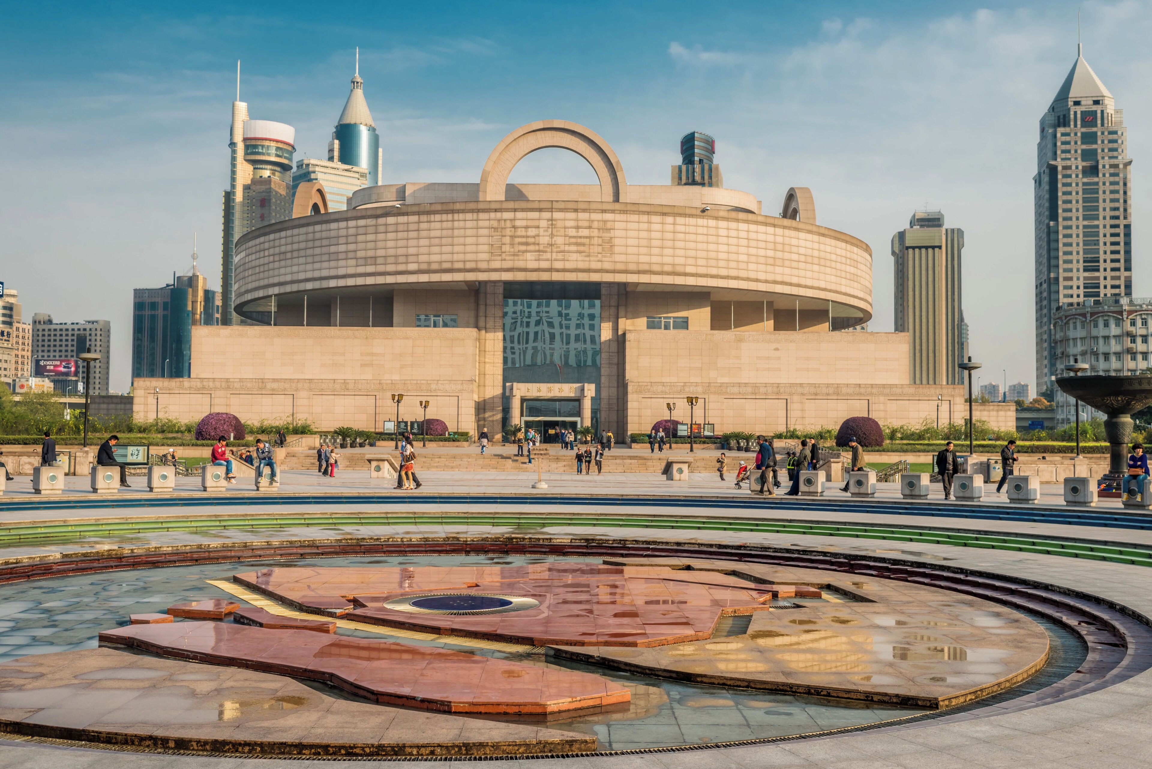 Un edificio grande y circular con una cúpula central y una plaza circundante con una fuente.