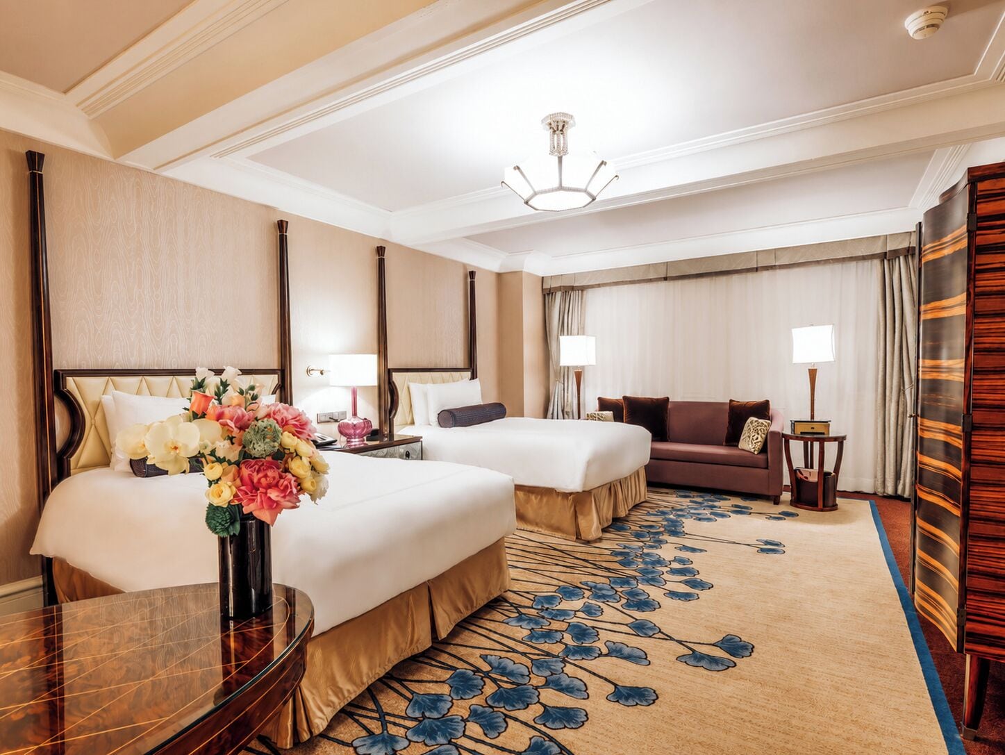 Ein Hotelzimmer mit zwei Betten, einem Sofa, einem Schreibtisch und einer Kristallleuchter.