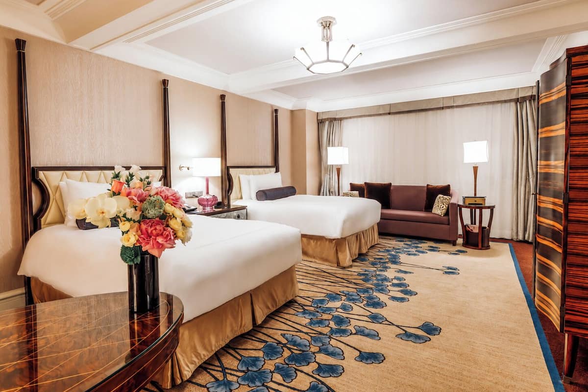 A hotel room with two beds, a sofa, a desk, and a chandelier.