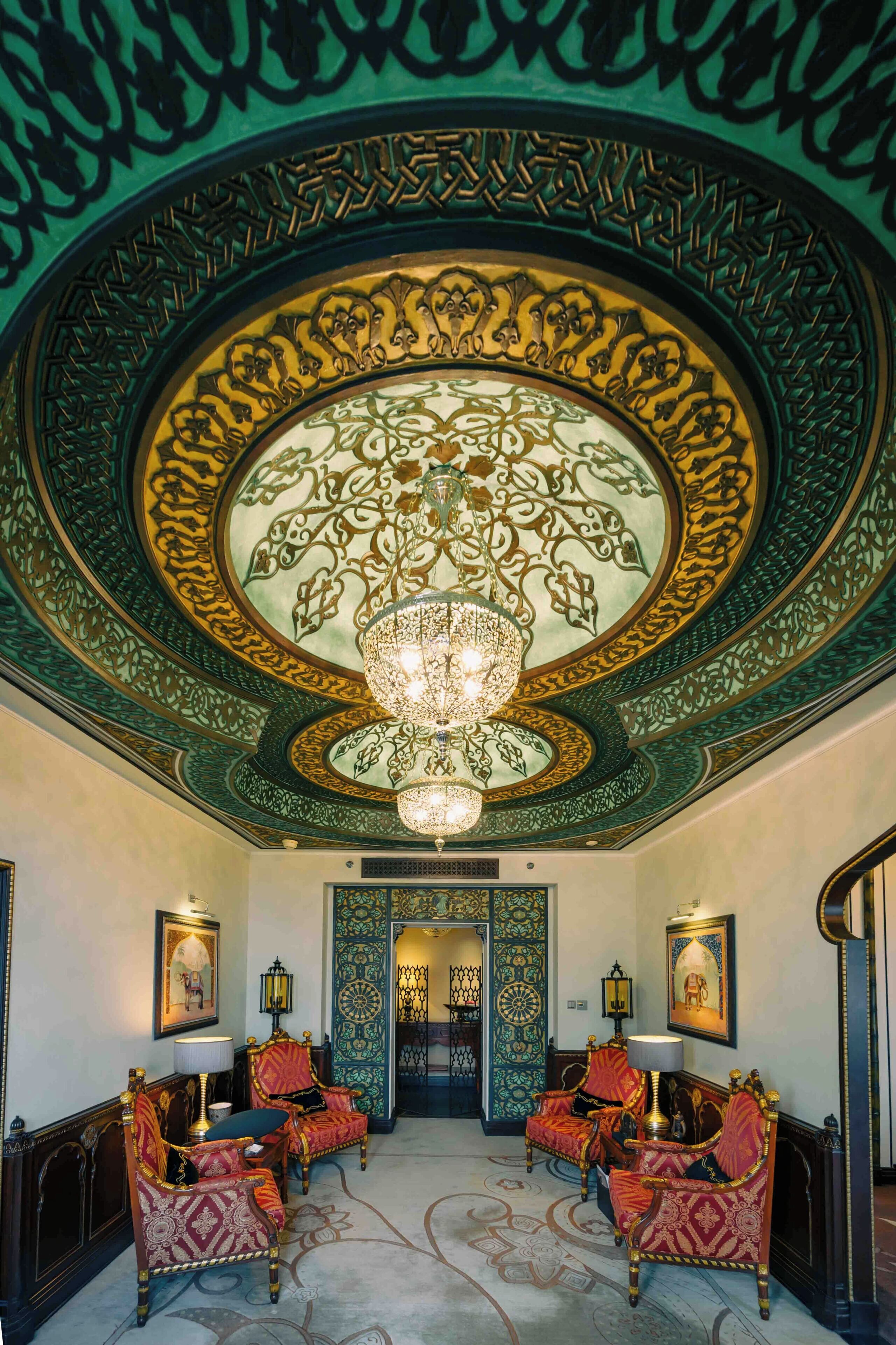 A lobby with ornate ceiling artwork, a chandelier, and seating with lamps.