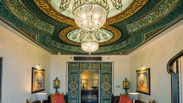 A lobby with ornate ceiling artwork, a chandelier, and seating with lamps.
