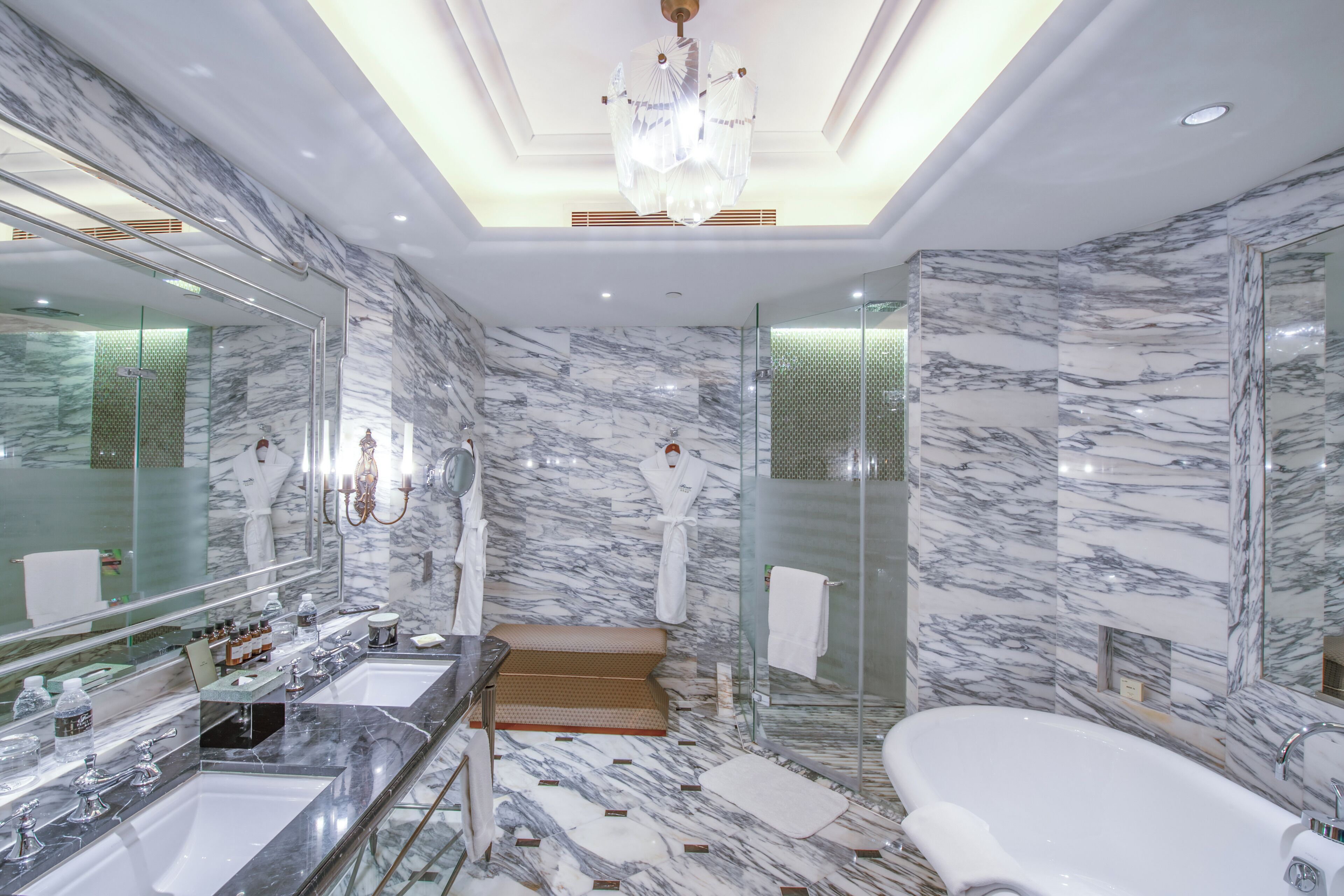A luxurious bathroom with marble walls, a large mirror, a bathtub, and a walk-in shower.