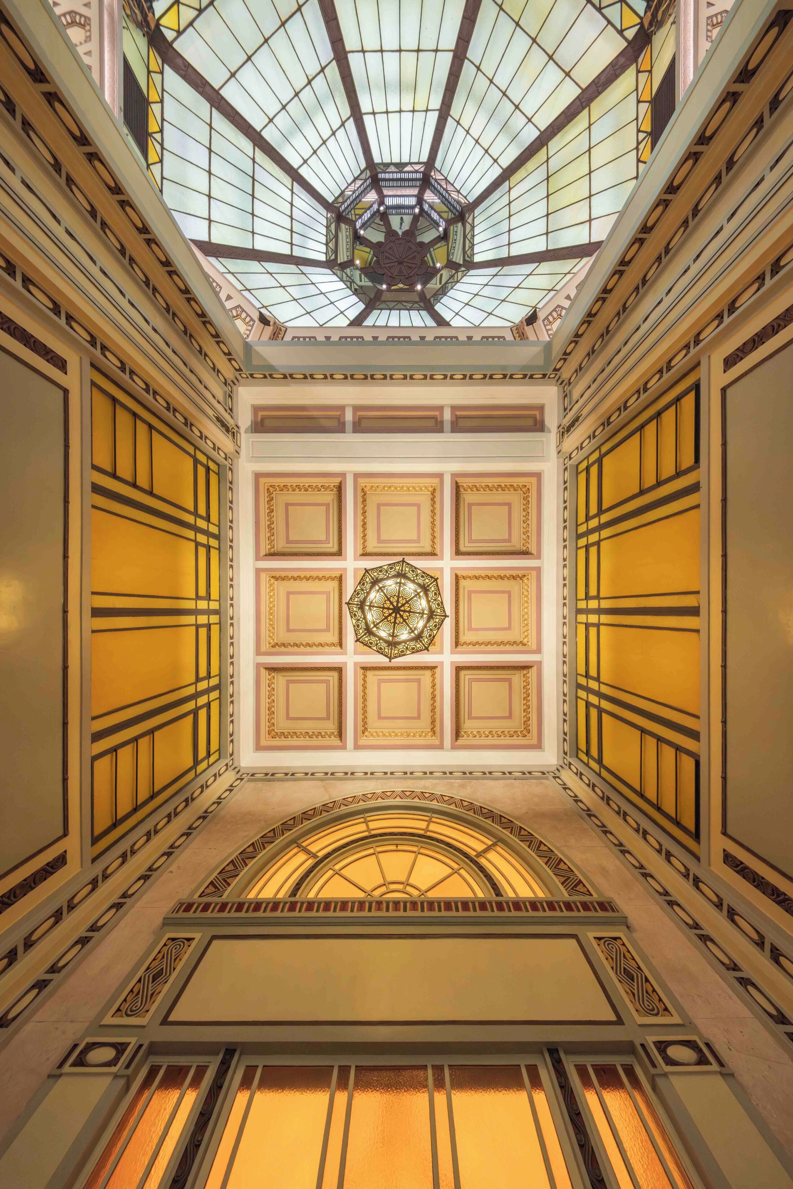 A grand interior with a glass ceiling, ornate wall panels, and a central decorative element.