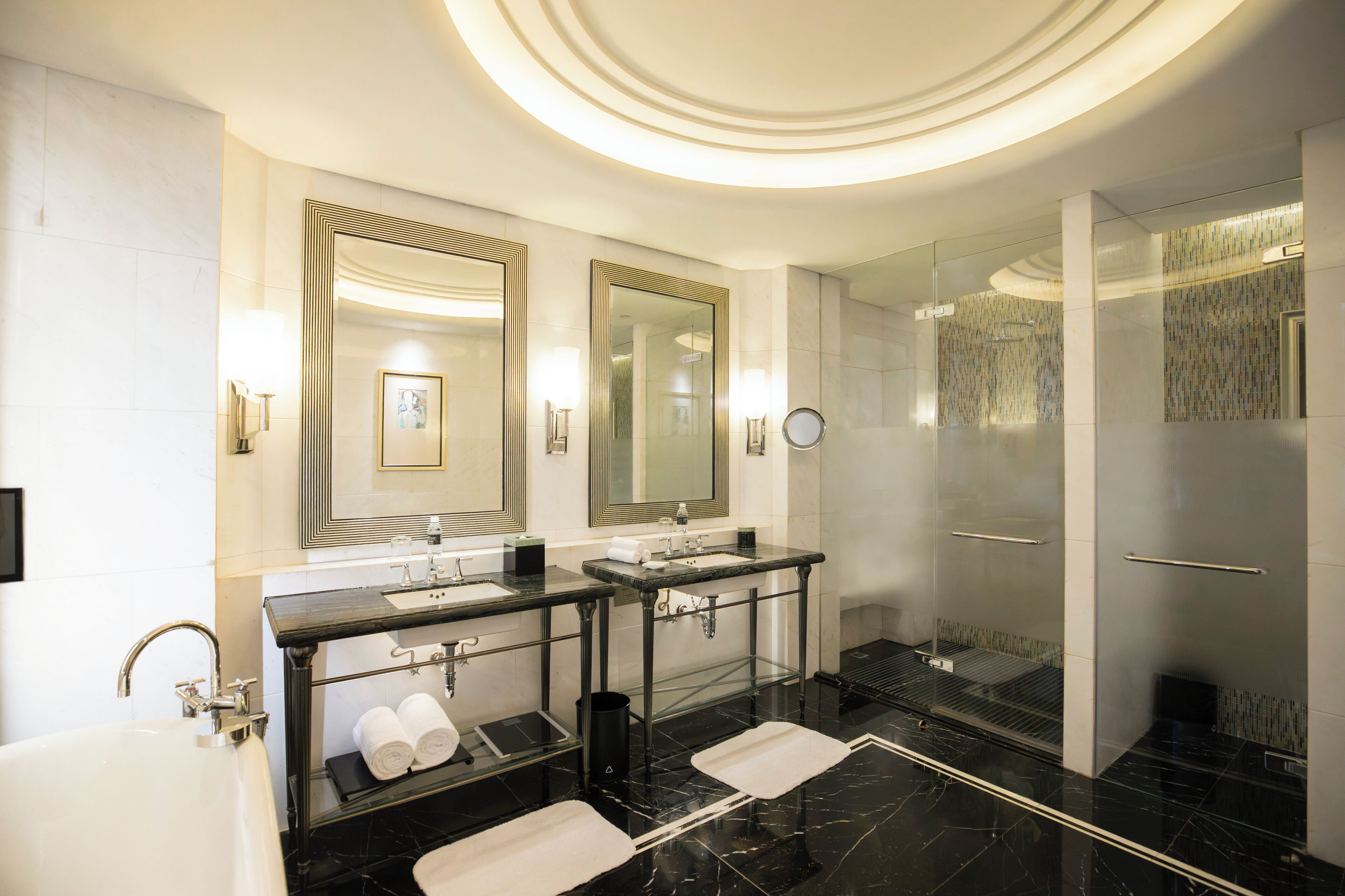Un bagno moderno con due lavabi, uno specchio grande, una vasca e una doccia in vetro.