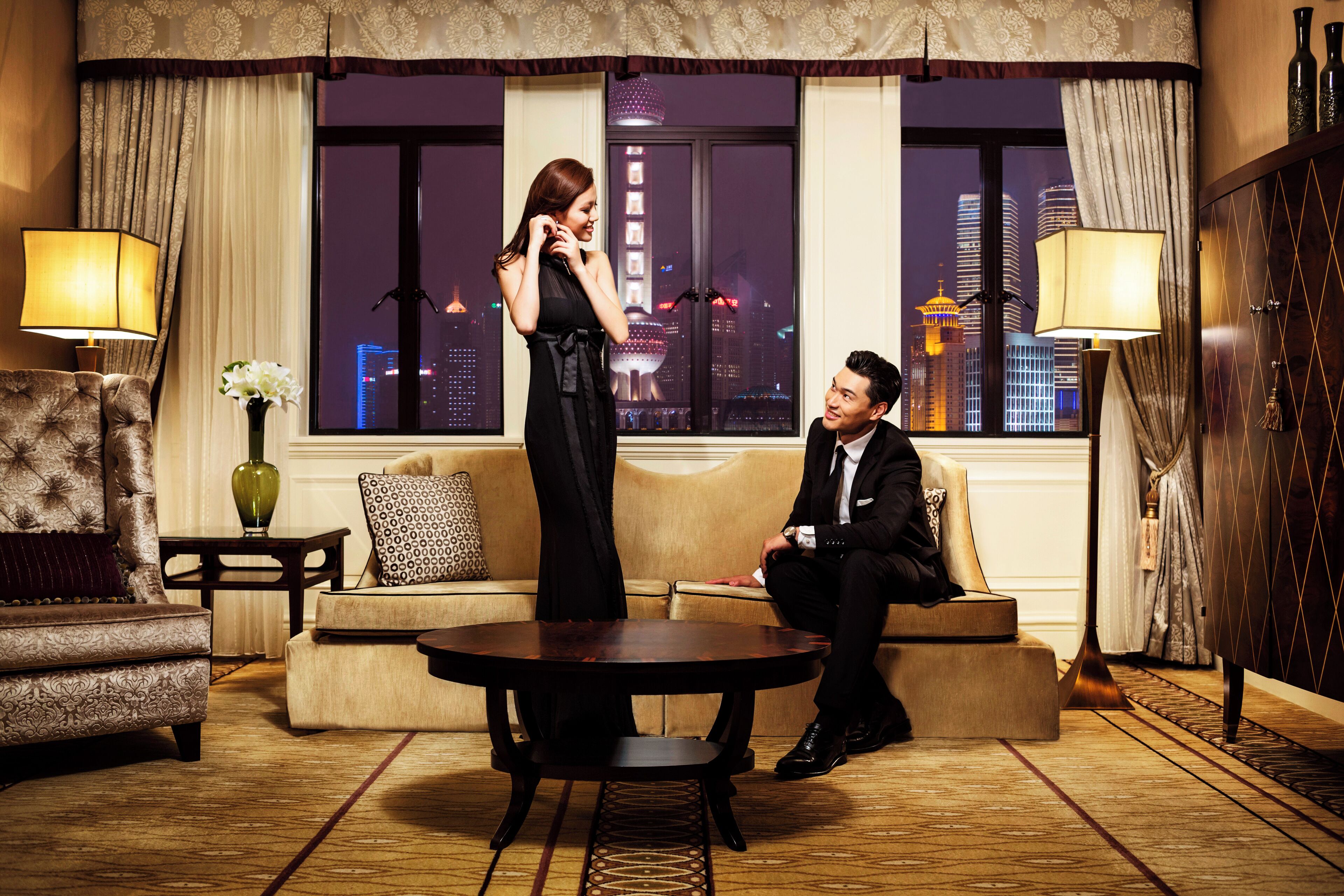 A hotel room with a city view, a sofa, a coffee table, and a lamp.