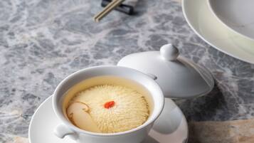 A cup of tea with a white teapot and saucer on a marble surface.