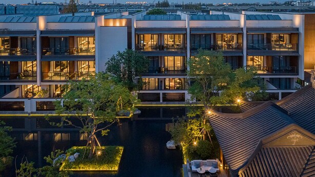 Un hotel moderno con varios pisos, un jardín en la azotea y una tranquila fuente de agua.
