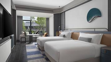 A hotel room with two beds, a TV, a dining area, and a view of the outdoors.