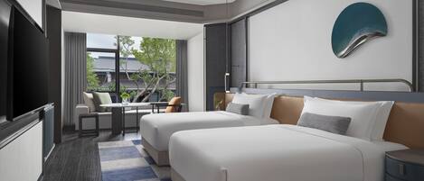 Habitación de hotel con dos camas, televisión, zona de comedor y vistas al exterior.