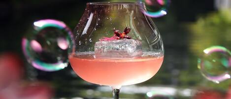 Un vaso de cóctel con una bebida rosada sobre un posavasos, rodeado de burbujas.