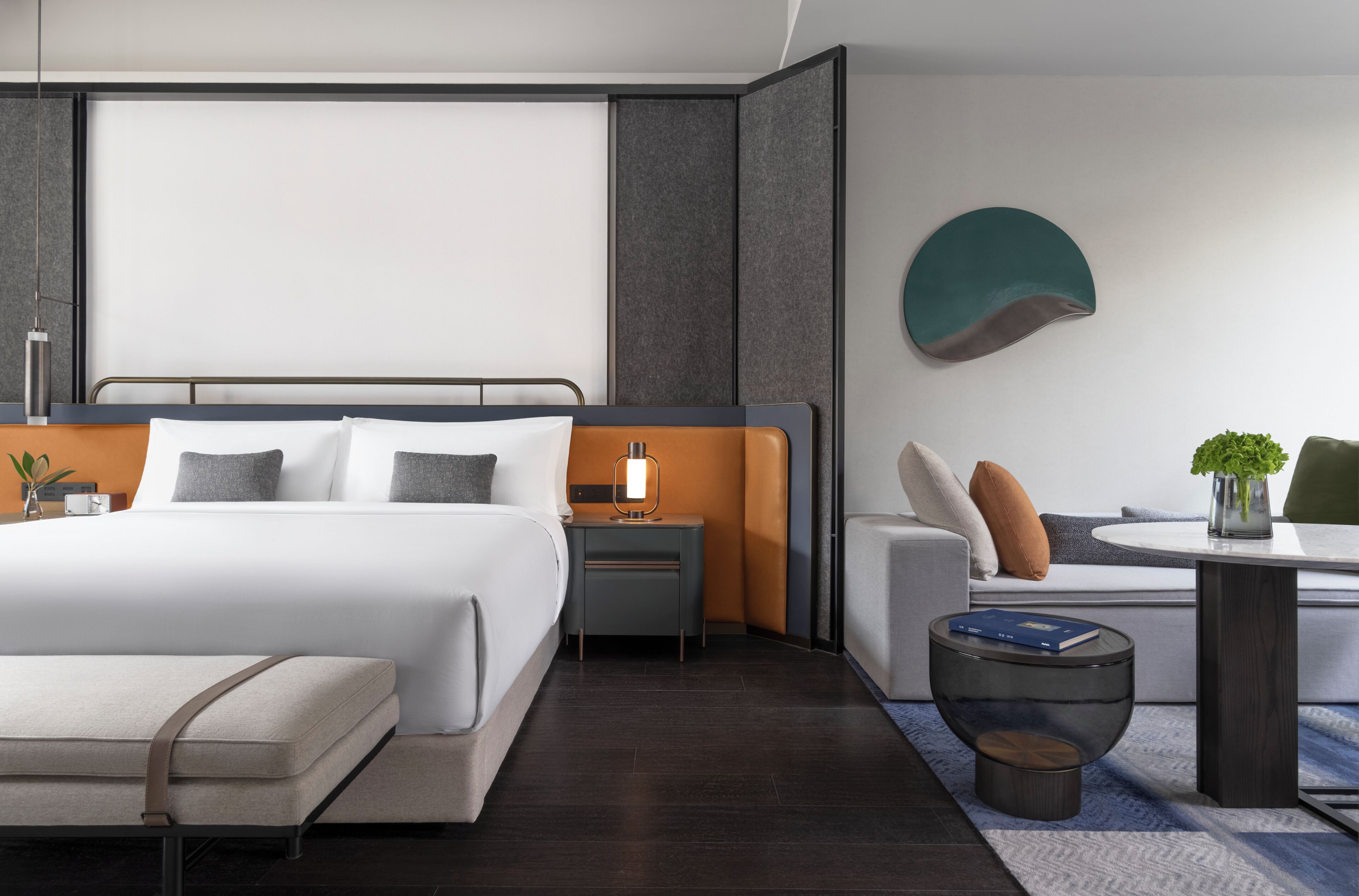 Una habitación de hotel moderna con cama, mesita de noche, zona de estar y una mesa redonda.