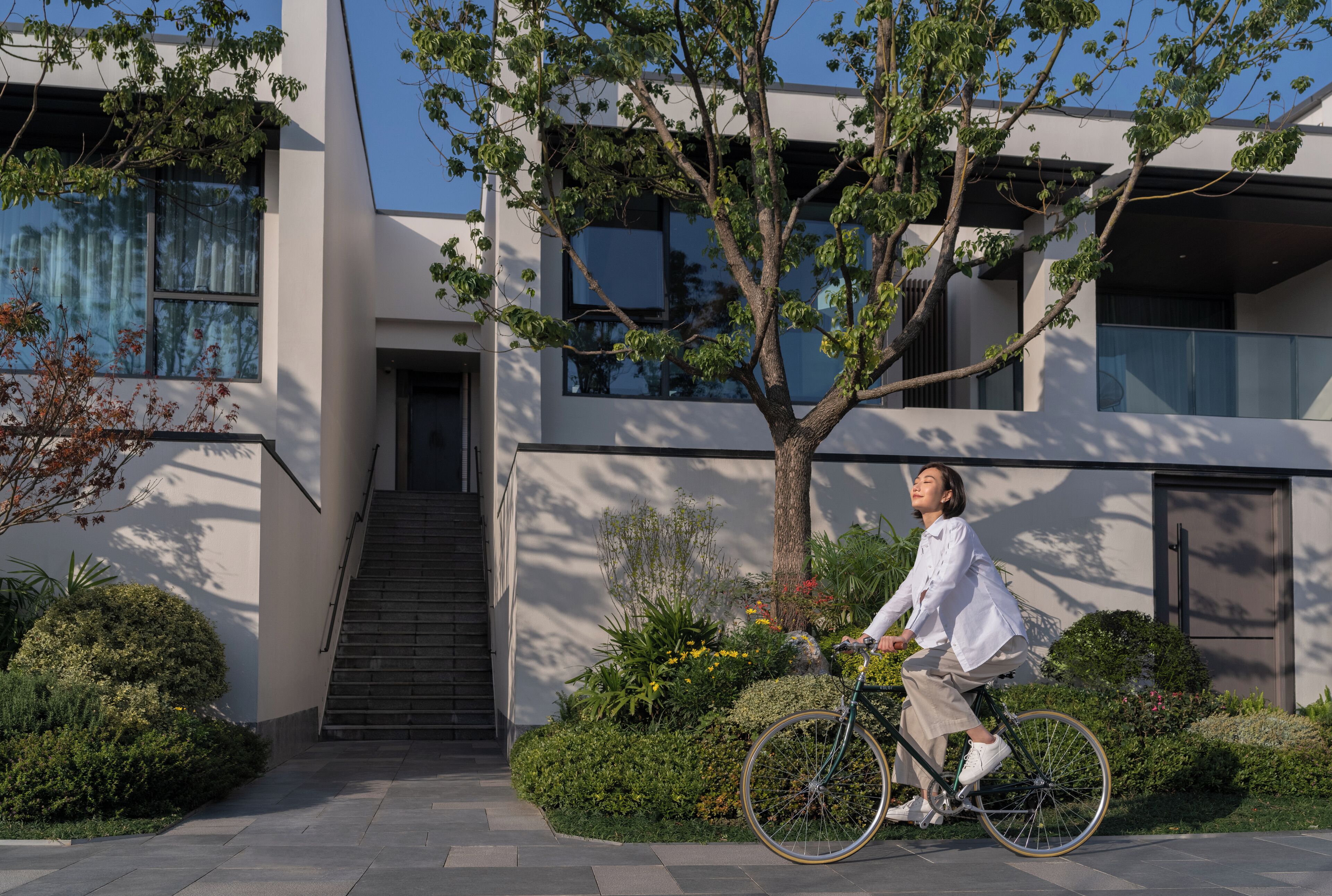 A modern building with a staircase, a tree, and a person riding a bicycle.