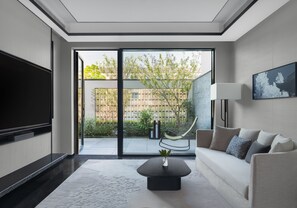 Ein modernes Wohnzimmer mit Flachbildfernseher, einer Couch, einem Couchtisch und einer großen Glasschiebetür, die zu einem Außenbereich mit Hängematte und Grünpflanzen führt.