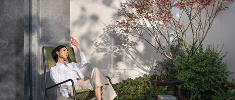 A person sitting on a chair in a modern outdoor setting with a potted plant and a stone bench.