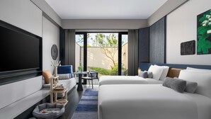 Una habitación de hotel moderna con una cama grande, un sofá, un televisor, una mesita y vistas al exterior.