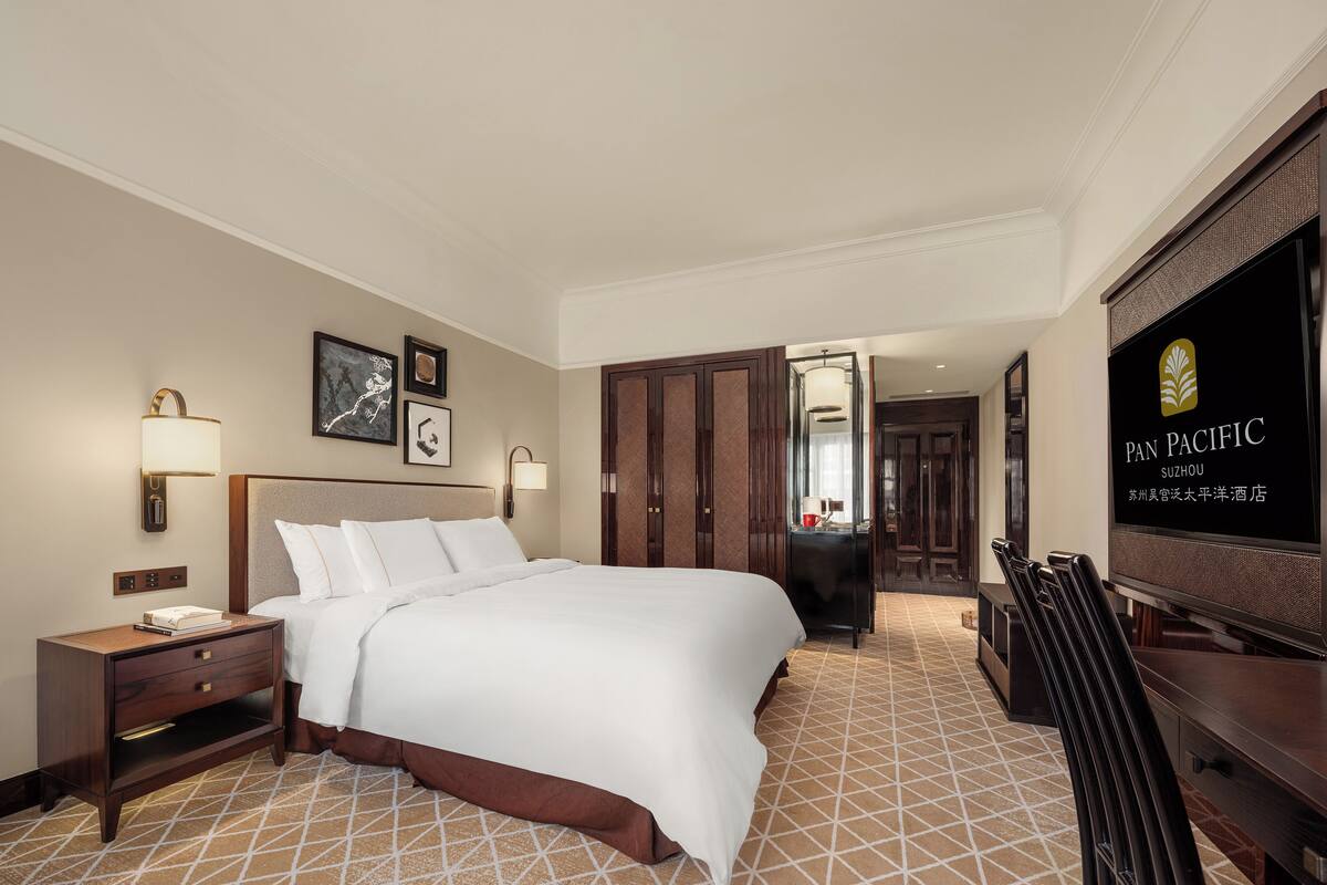 A hotel room with a large bed, bedside tables, a TV, and a mirror.
