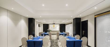 A conference room with a long table, chairs, and a projector screen at the front.