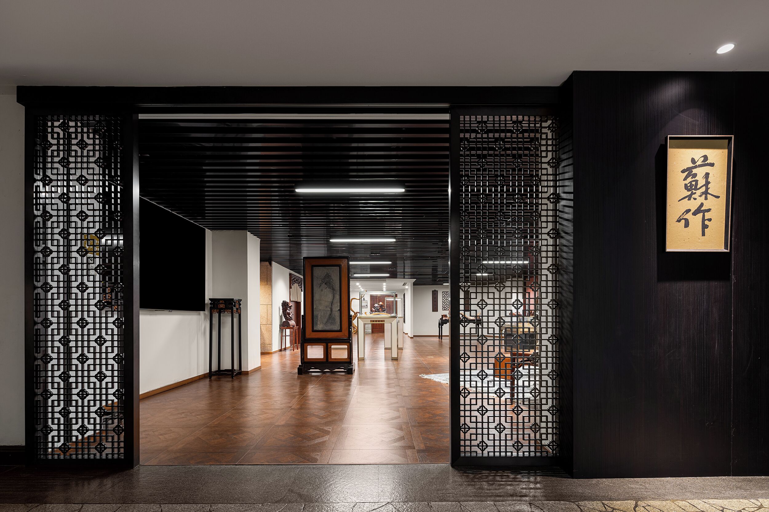 Un couloir à la décoration traditionnelle, comprenant des paravents aux motifs noir et blanc, un plancher en bois et une œuvre calligraphique encadrée accrochée au mur.