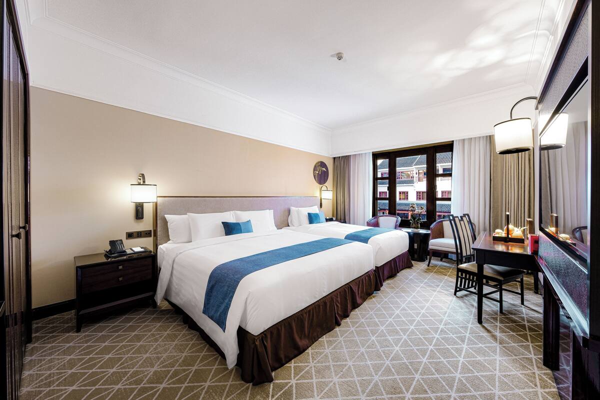 A hotel room with two beds, a desk, a chair, a TV, and a window with curtains.