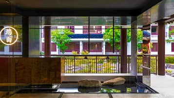 Experience the tranquil atmosphere of our lobby, featuring a reception desk with a glass partition, a stunning neon sign, and a serene water feature surrounded by lush greenery.