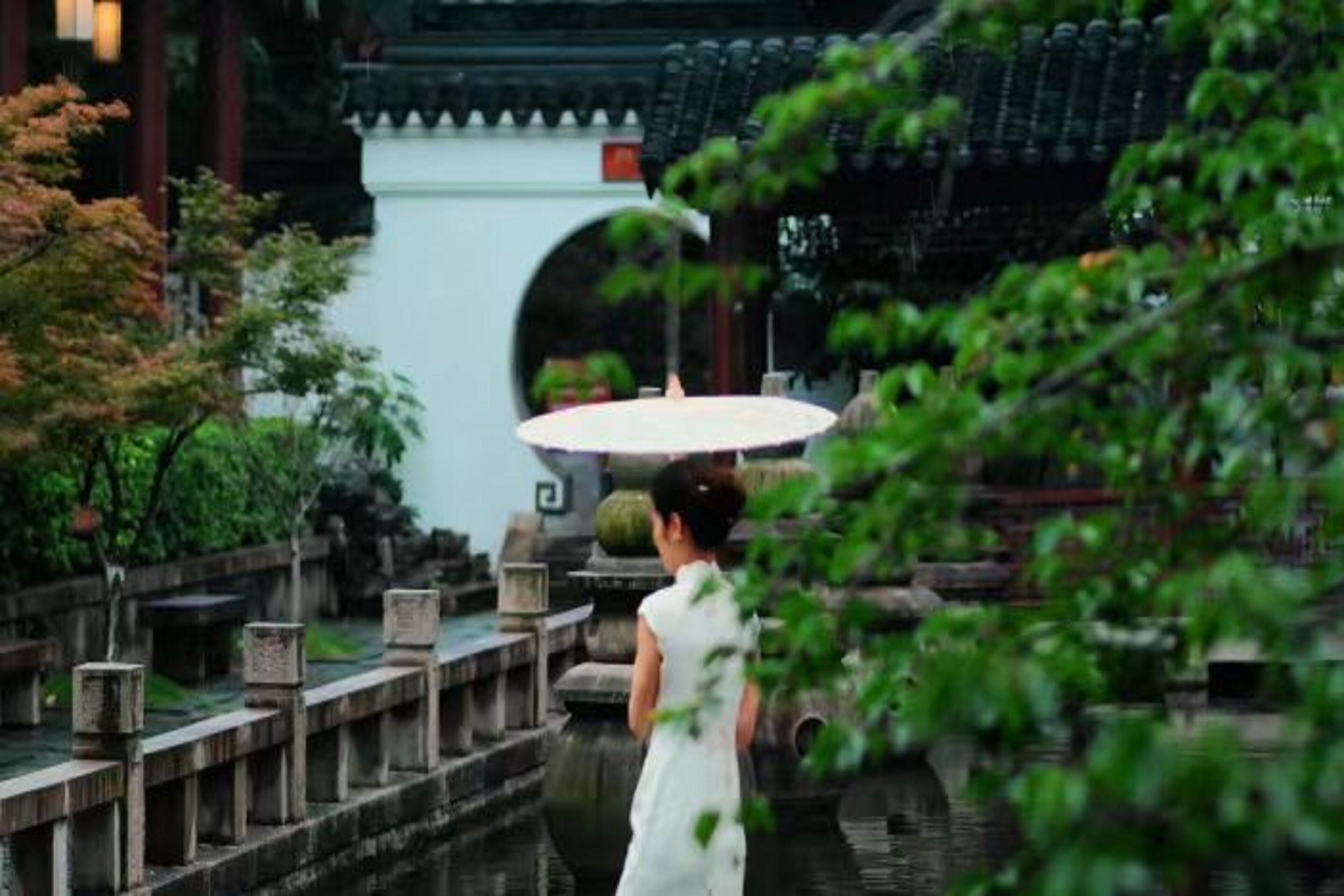 A traditional Chinese garden with a stone bridge, a pond, and a pavilion.