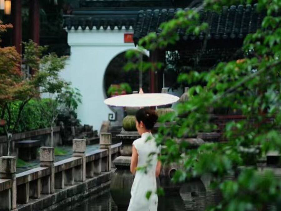 A traditional Chinese garden with a stone bridge, a pond, and a pavilion.