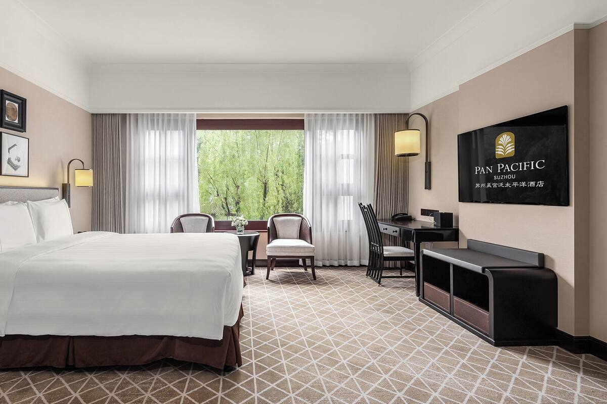 A hotel room with a bed, a desk, a chair, a TV, and a window with curtains.