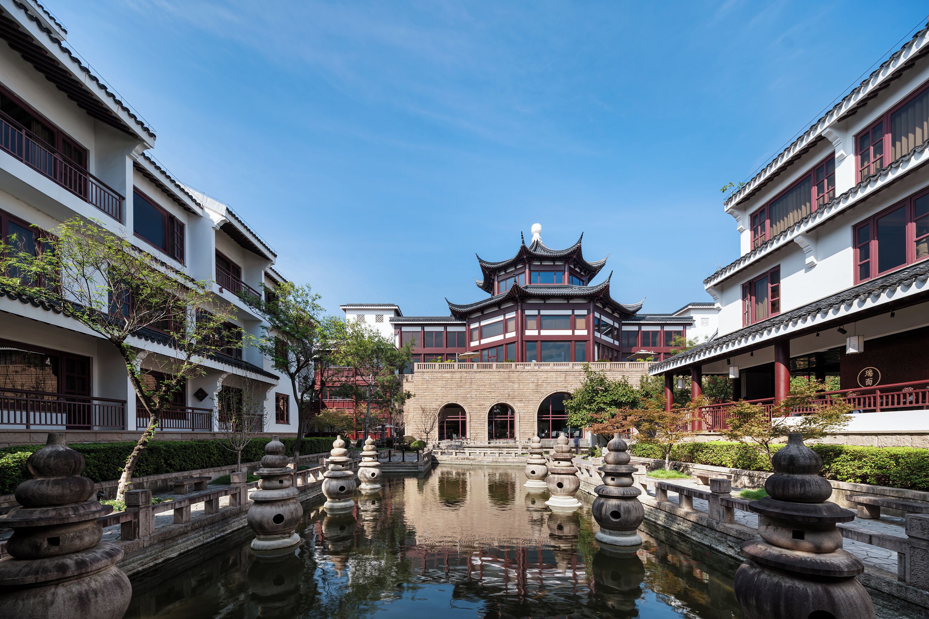 A traditional courtyard with a central pond, stone lanterns, and a multi-tiered building with a pagoda-style roof.