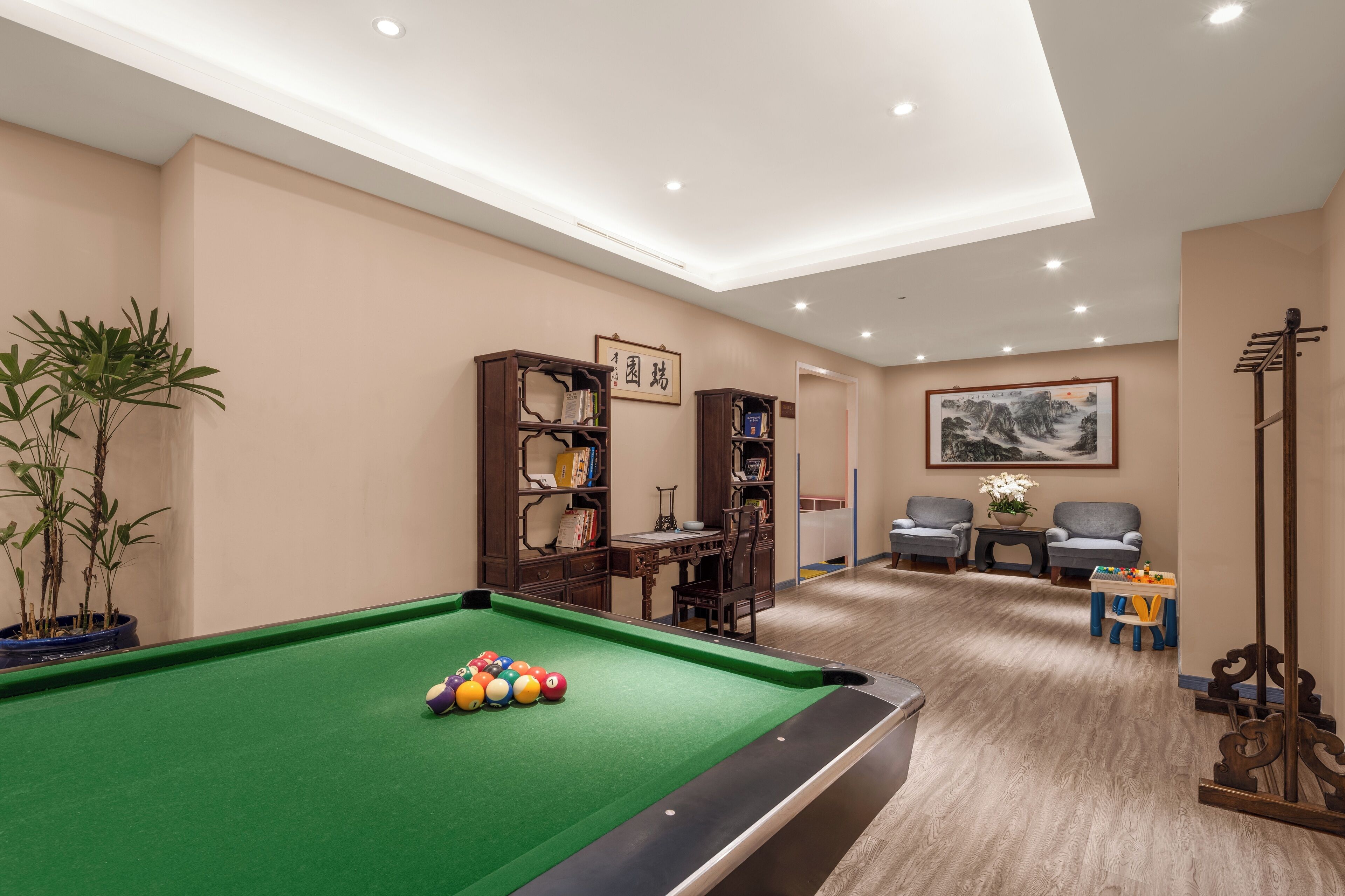 Una sala de billar con mesa de pool, estanterías, un escritorio y dos sillones.