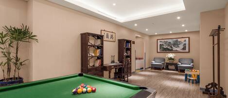 Una sala de billar con mesa de pool, estanterías, un escritorio y dos sillones.