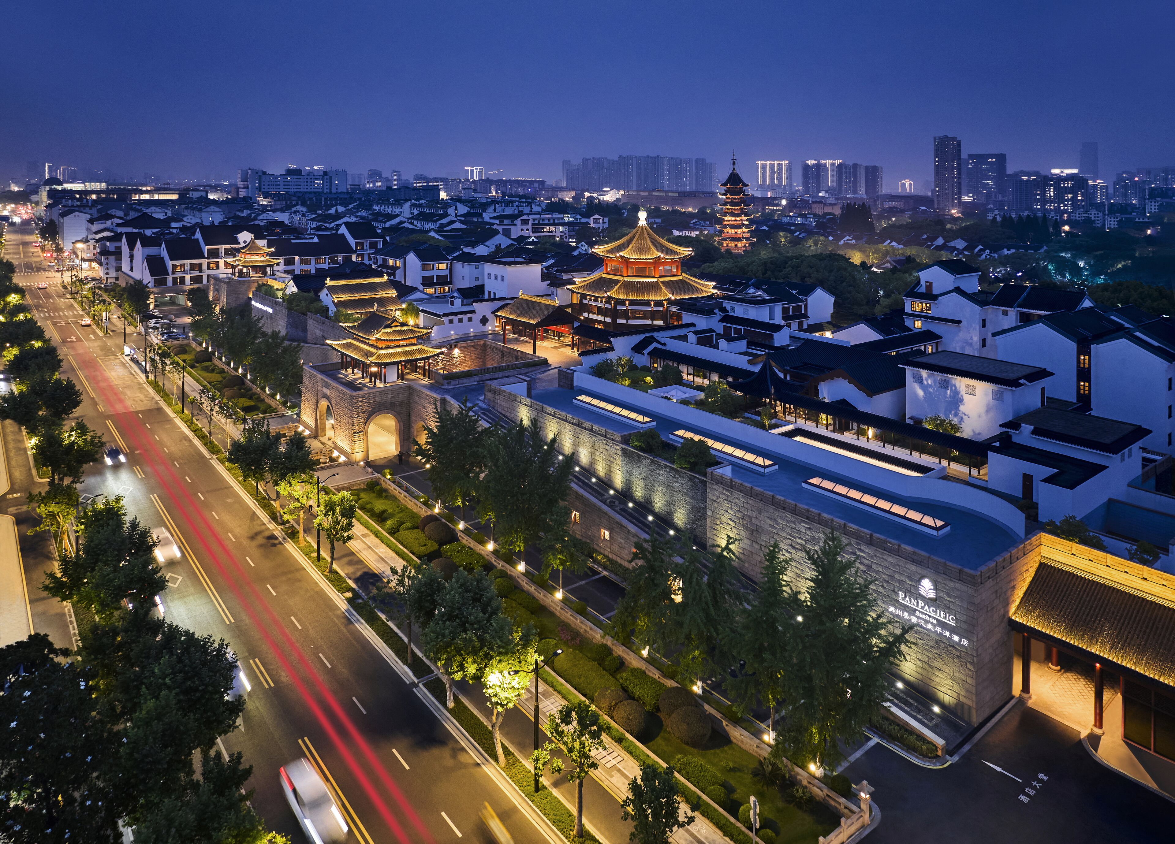 A traditional Chinese architectural complex with multiple pagoda-style buildings, a modern hotel structure, and a well-maintained road with traffic lights.