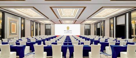 A conference room with rows of tables and chairs, a large screen displaying the logo, and a patterned carpet.