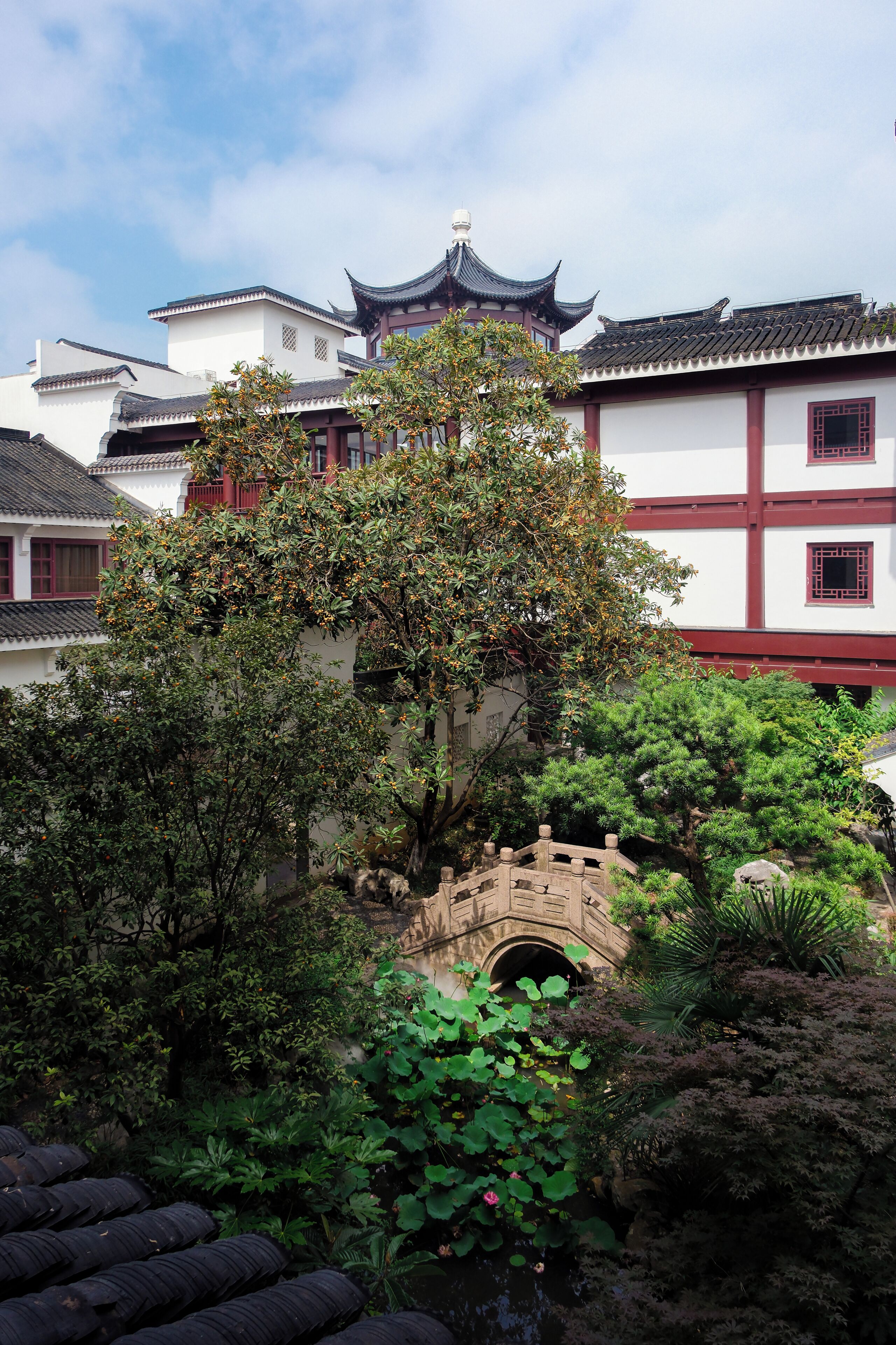 A traditional courtyard with a stone bridge, lush greenery, and classic architecture.