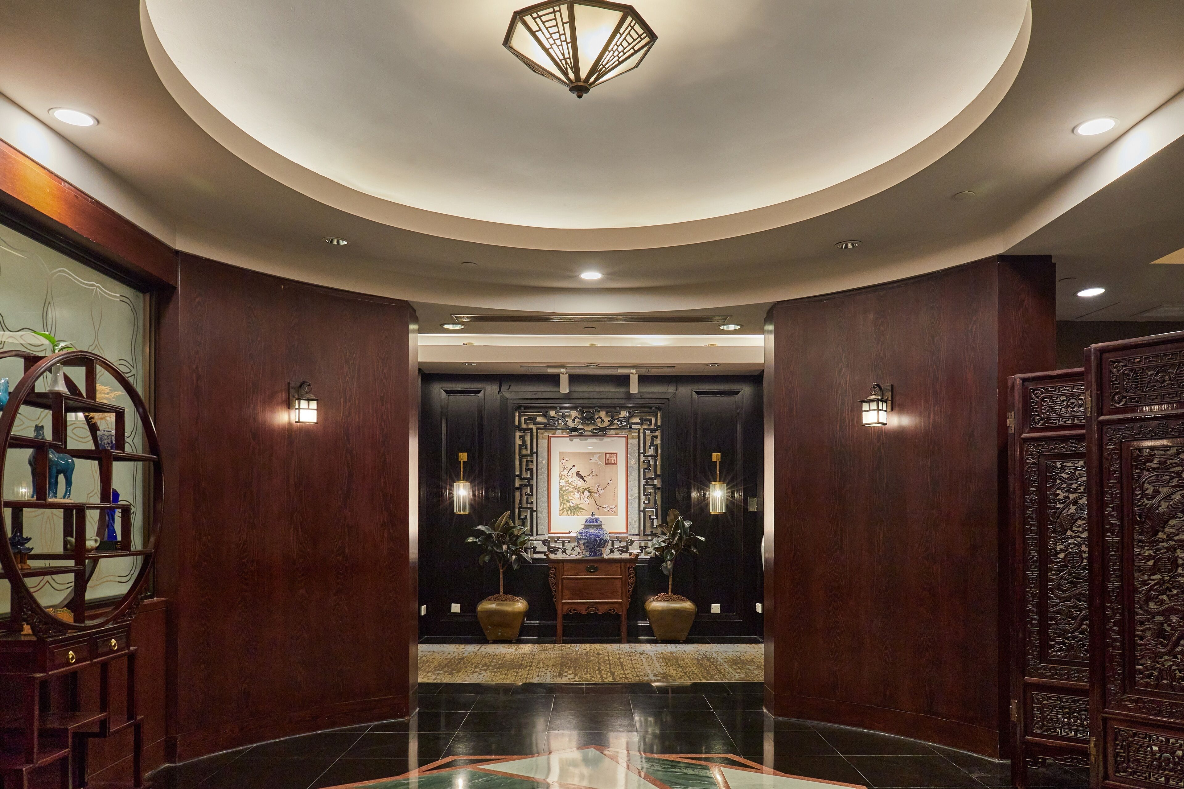 A lobby with a round ceiling, a central console table, two potted plants, and a decorative screen.