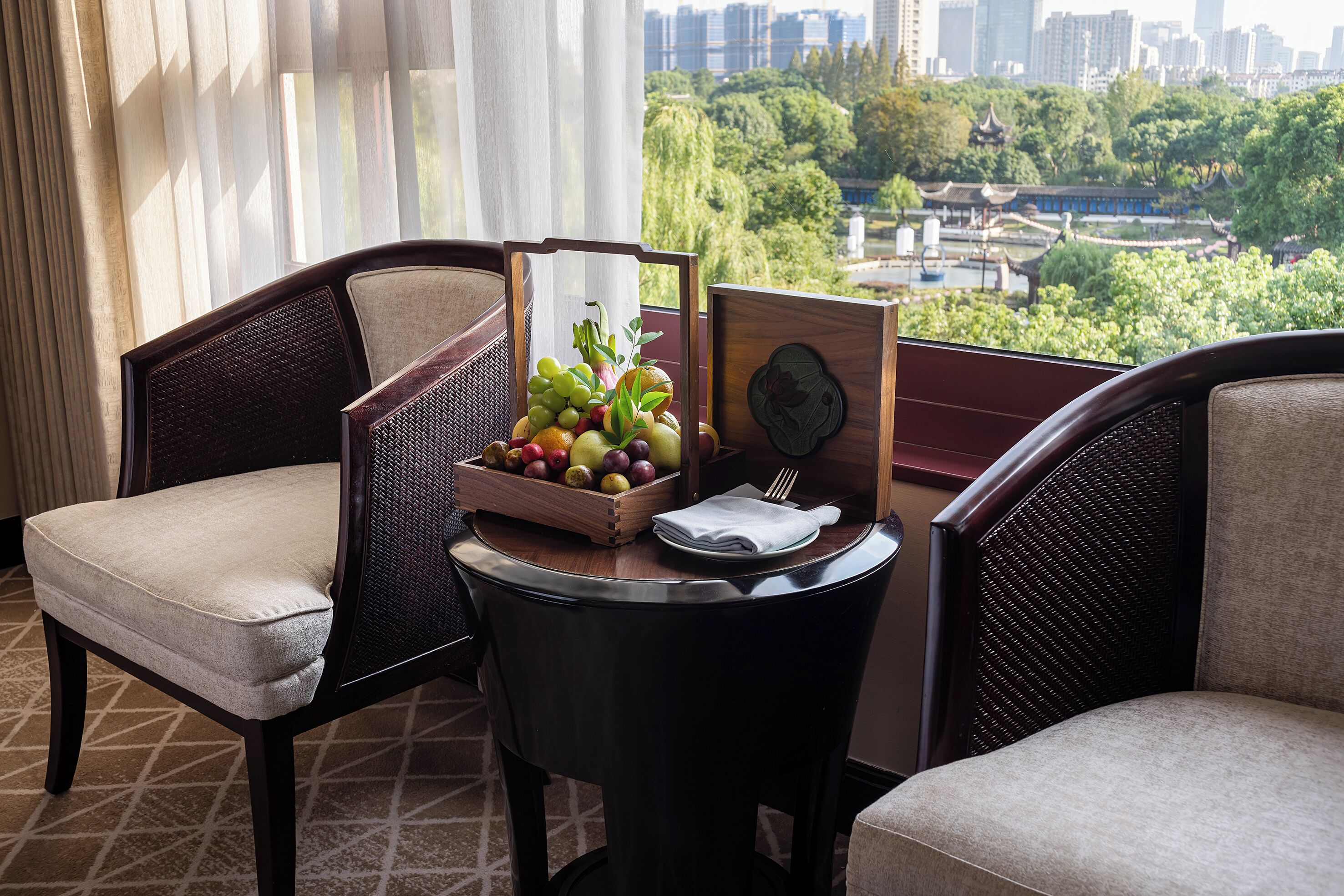 A balcony with two wicker chairs, a small table with a fruit basket, a folded napkin, and a decorative wooden plaque.