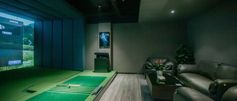 Ein modernes Zimmer mit einem Bereich aus grüner Kunstrasen, einer Ledersofa, einer Projektionsleinwand und einem kleinen Tisch mit einer Pflanze.