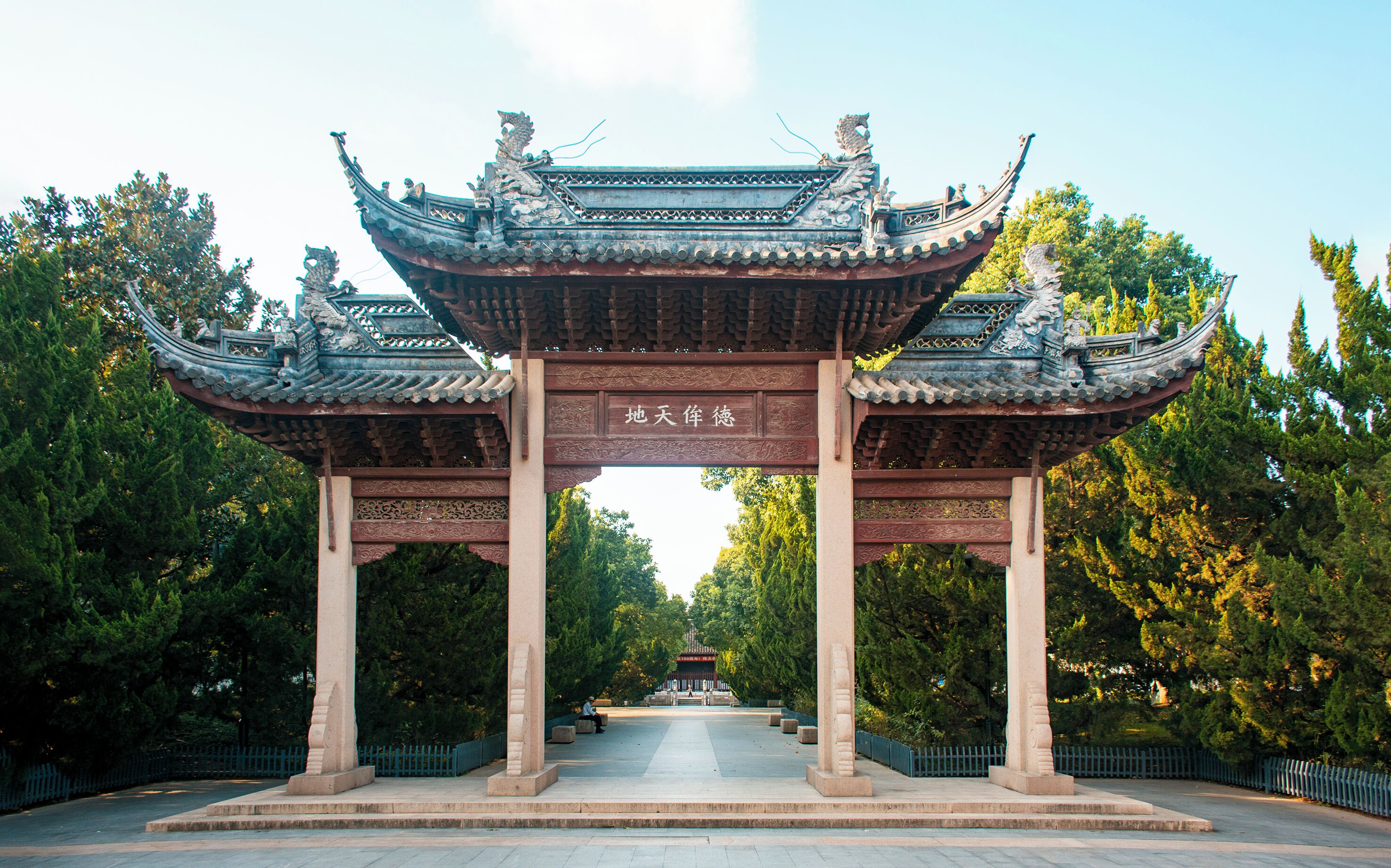 A traditional Chinese pavilion with ornate roof and columns, surrounded by trees.