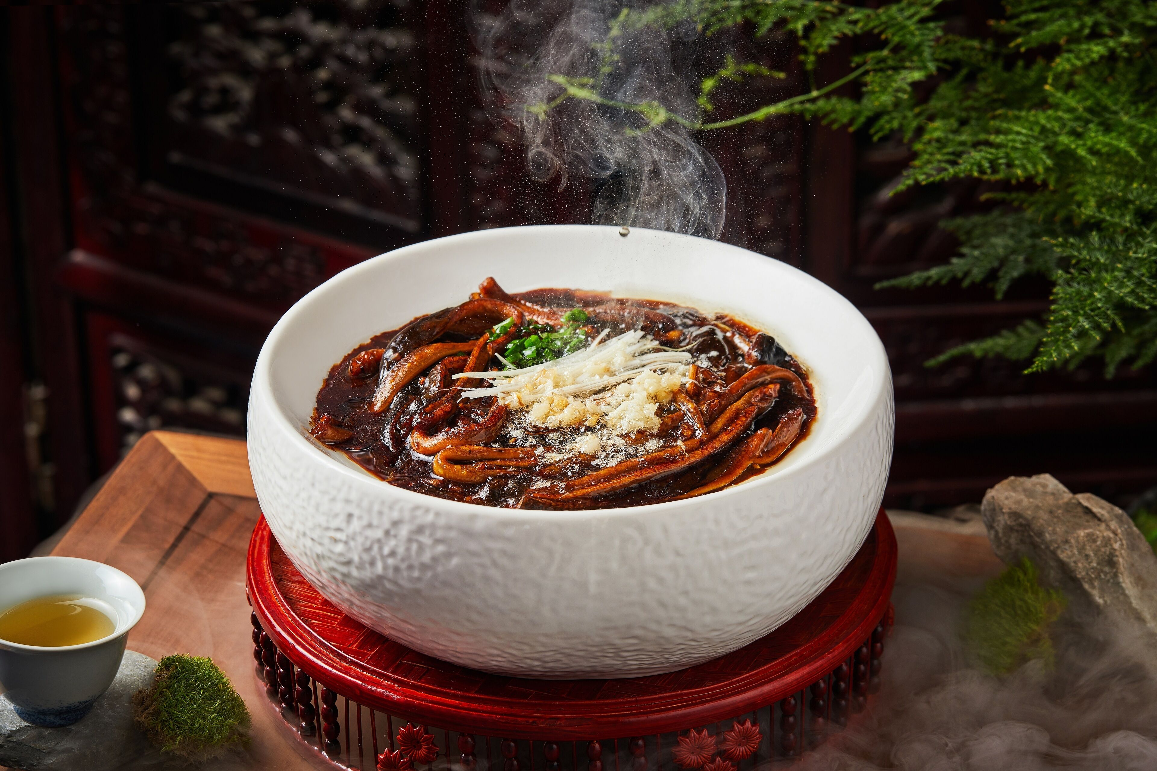 A bowl of hot soup with steam rising, served on a red stand.