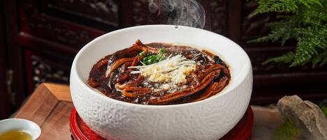 A bowl of hot soup with steam rising, served on a red stand.