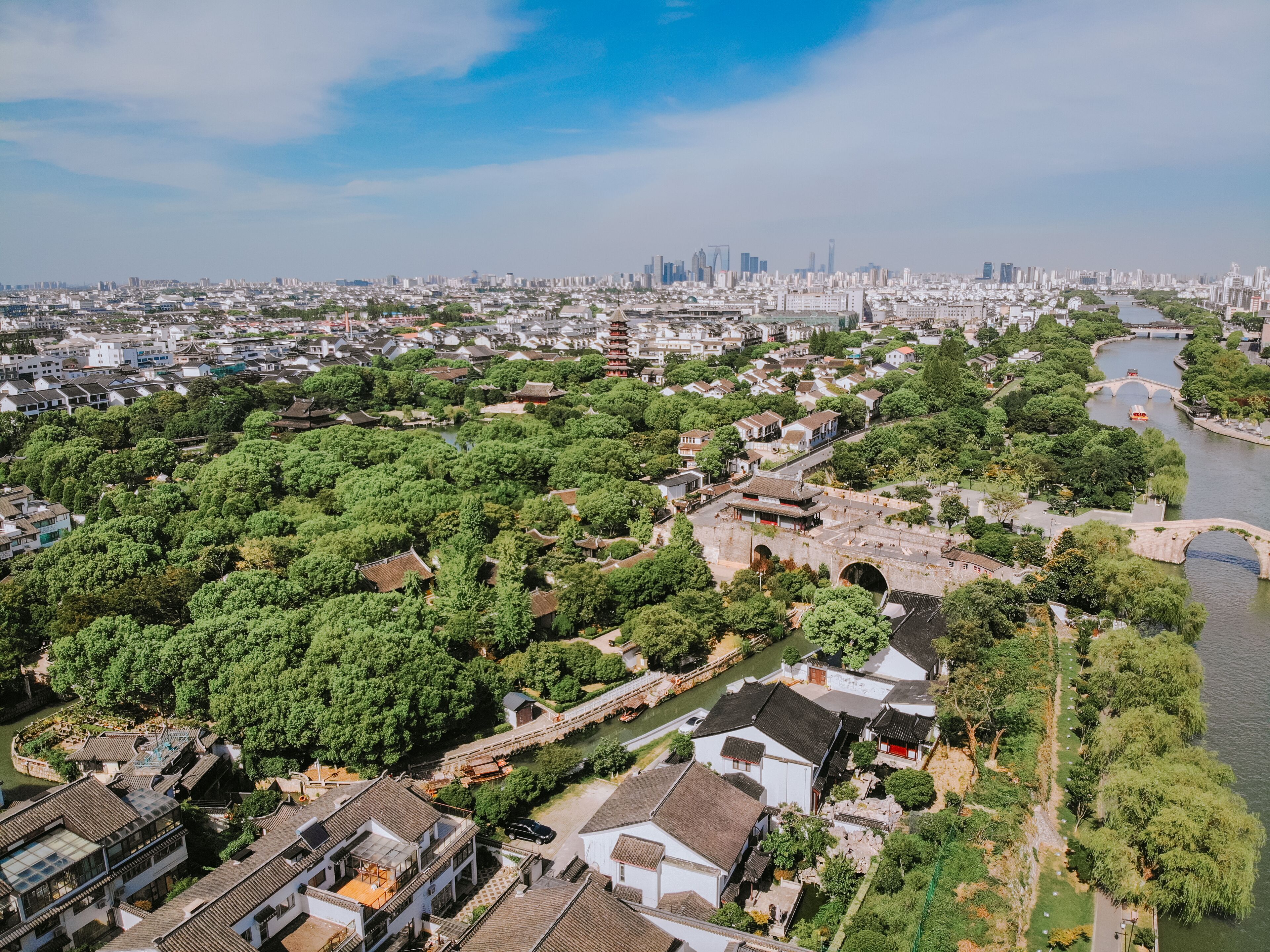 Vista aérea de un pueblo tradicional con abundante vegetación, un río y una combinación de edificios antiguos y modernos.